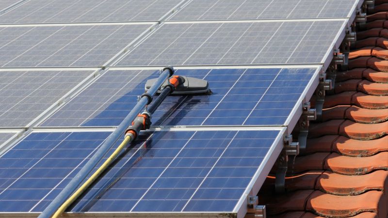 Photovoltaikanlage auf dem Dach: ein Solarmodul wird mit einem speziellen Gerät von Staub befreit.