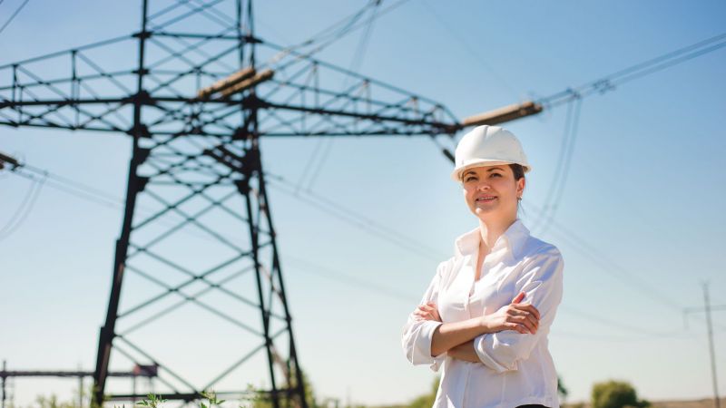 Symbolbild: Eine Ingenieurin steht vor einem Strommast.