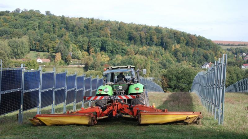 Traktor fährt auf Feld mit Solarmodulen
