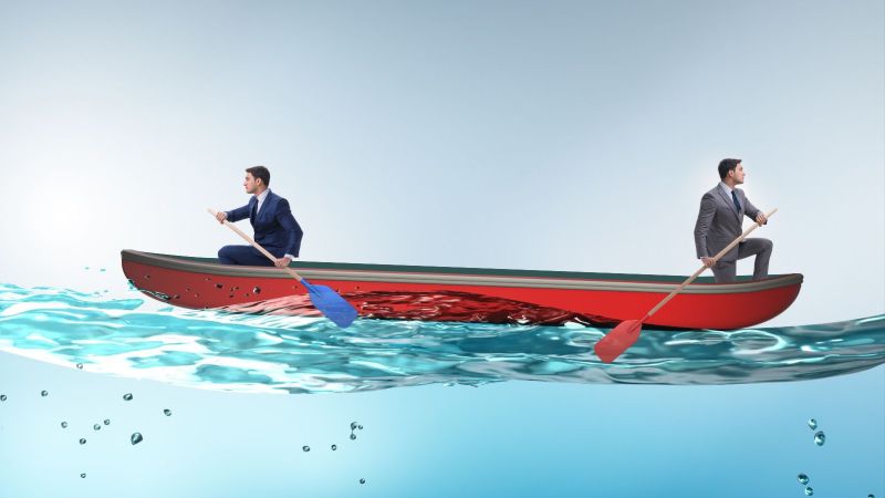 Zwei Männer sitzen in einem Boot und paddeln in entgegengesetzte Richtungen