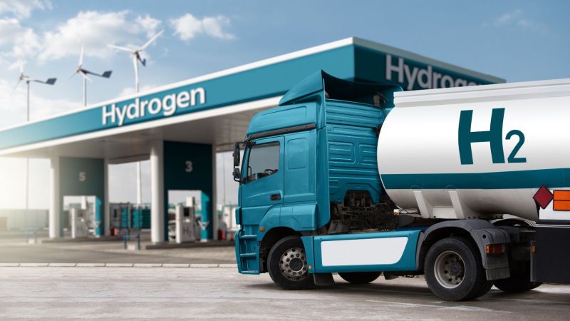 LKW mit Wasserstofftankanhänger vor dem Hintergrund einer H2-Tankstelle 