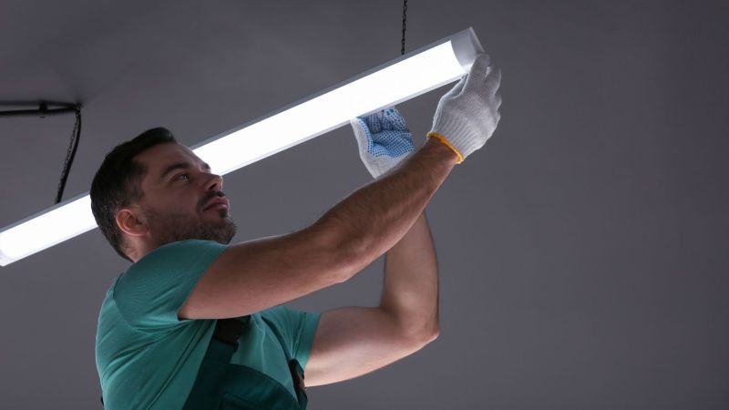 Ein Mann installiert eine LED-Leuchtstoffröhre an einer Decke.